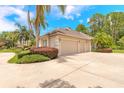 Three-car garage with a concrete driveway, lush landscaping, and mature palm trees at 15 Cambridge Trce, Ormond Beach, FL 32174