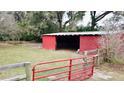 View of a red barn with a gate, in a wooded area at 13660 Se 80Th Ave, Summerfield, FL 34491