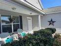 Close up of the inviting front porch, decorated with a floral wreath, seating, and lovely greenery at 2595 Edenville Path, The Villages, FL 32162