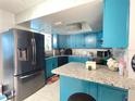Modern kitchen with stainless steel appliances, granite countertops, mosaic backsplash, and vibrant blue cabinets at 10867 Sw 83Rd Ct, Ocala, FL 34481