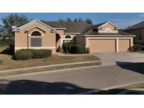 Tan house with three-car garage and lush landscaping at 510 Coventry Rd, Davenport, FL 33897