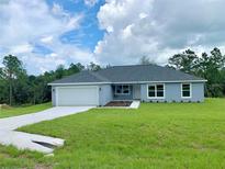 Newly constructed home with gray siding, a two-car garage, and a well-manicured lawn at 6435 Sw 204 Ave, Dunnellon, FL 34431