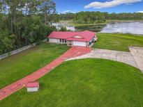 Aerial view of a home with a red metal roof, a long driveway, and a lakeside backyard at 318 Mitnik Dr, Deltona, FL 32738