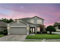 Charming two-story home with a well-manicured lawn, a brick driveway, and a two-car garage under a colorful sky at 1485 Waukon Cir, Casselberry, FL 32707