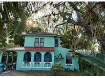 Charming two-story home with a light green exterior, a red roof, arched windows, and lush, mature landscaping at 110 Ingleby Se Dr, Winter Haven, FL 33880