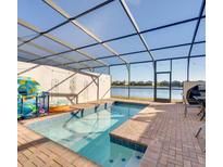 Relaxing screened pool area boasts blue tiled pool, brick pool deck, and lake views at 8882 Geneve Ct, Kissimmee, FL 34747