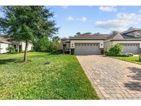 Two-story house with gray roof and brick paver driveway, surrounded by lush landscaping at 830 Aldenham Ln, Ormond Beach, FL 32174