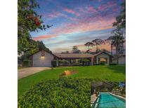 Beautiful single-story home with a well-manicured lawn, complemented by a lovely pool area and picturesque sunset sky at 75 Knollwood Estates Dr, Ormond Beach, FL 32174