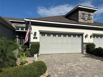 Home exterior showcasing a two-car garage, a stone facade, and a well-manicured front yard with a flag at 745 Aldenham Ln, Ormond Beach, FL 32174