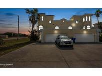 Beige two-story house with a two-car garage, palm trees, and wide driveway at dusk at 3074 Ocean Shore Blvd, Ormond Beach, FL 32176