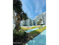 Beautiful resort pool with deck seating, surrounded by lush tropical greenery and condominium building at 2727 N Atlantic Ave # 602, Daytona Beach, FL 32118