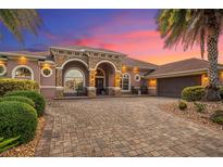 Stunning home with a brick driveway, archway entrance, and lush tropical landscaping and palm trees at sunset at 568 Luna Bella Ln, New Smyrna Beach, FL 32168