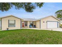 Charming single-story home with a well-maintained lawn and attached garage, accented by blue trim and a red front door at 2910 Yule Tree Dr, Edgewater, FL 32141