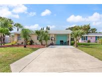 Tan single story home with teal garage door, landscaping, and long driveway at 48 Palm Dr, Ormond Beach, FL 32176