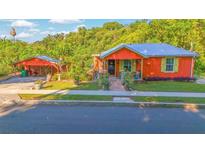 Charming orange home with a blue metal roof, lush landscaping, and a detached garage at 151 S Clayton St, Mount Dora, FL 32757