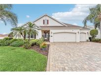 Attractive single-story home with a paver driveway, three-car garage, well-kept lawn, and beautiful tropical landscaping at 1596 Birmingham Ter, The Villages, FL 32162