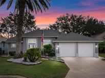 Charming home featuring a two-car garage, manicured lawn, landscaping, and mature palm tree at dusk at 20744 Queen Alexandra Dr, Leesburg, FL 34748