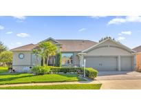 Charming single-story home featuring a manicured lawn, mature landscaping, and a three-car garage at 3530 Mulberry Grove Loop, Leesburg, FL 34748