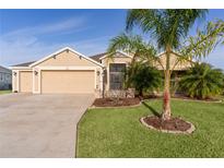 Tan house with three-car garage, lush landscaping, and palm trees at 3113 Sweetgum St, The Villages, FL 32163