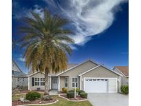 Tan house with white garage door and palm tree at 2219 Welcome Way, The Villages, FL 32162