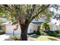 Single-story home with brick facade and attached garage, nestled amongst mature trees at 24947 Cranes Roost Cir, Leesburg, FL 34748