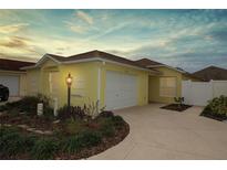 Bright yellow house with a two-car garage and well-manicured landscaping at 2078 Pink Blossom Ct, The Villages, FL 32162