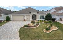 Tan house with landscaped yard, 3-car garage, and paver driveway at 2096 Odessa Cir, The Villages, FL 32162