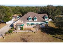 Charming home boasts a covered porch, manicured lawn, stone accents, and mature trees at 37008 Shalimar Dr, Fruitland Park, FL 34731