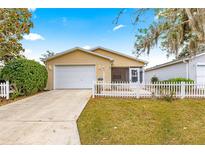 Cute yellow house with white picket fence, garage, and driveway at 453 Hildalgo Dr, Lady Lake, FL 32159