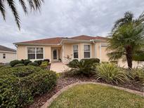 Tan one-story home with brown roof, landscaped yard, and two-car garage at 364 Kilmer Way, The Villages, FL 32162