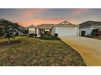 Charming single-story home featuring a well-manicured lawn, a two-car garage, and a serene sunset backdrop at 507 Delfin Rd, The Villages, FL 32163