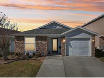Charming single-story home with brick accents, attached garage, and well-maintained lawn against a colorful sunset sky at 12306 Ne 48Th Way, Oxford, FL 34484