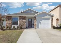 Charming single-Gathering home featuring a stone facade, well-maintained lawn, and attached garage at 12306 Ne 48Th Way, Oxford, FL 34484