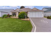 Tan one-story house with a two-car garage and landscaped lawn at 2240 Avon Loop, The Villages, FL 32162