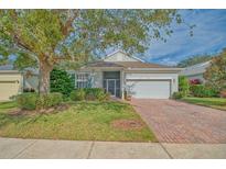 Single-story home with brick driveway, lush landscaping, and a large tree in the front yard at 2298 Caledonian St, Clermont, FL 34711