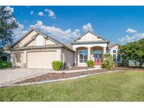 Tan house with red front door, landscaping, and a paved driveway at 2441 Bar Harbor Bay, Mount Dora, FL 32757