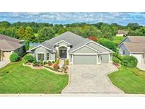 One-story house with a green facade, paver driveway, and landscaped lawn at 2532 Edenville Path, The Villages, FL 32162