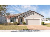 Tan one-story house with brown roof, two-car garage, and landscaping at 2029 Sloans Outlook Dr, Groveland, FL 34736