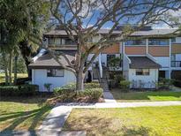 Exterior view of a two-story condo building with a large tree and landscaping at 4668 Tower Pine Rd # Ge, Orlando, FL 32839