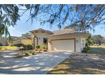 Single-story home with light beige walls, a two-car garage, and a brick driveway at 6027 Spinnaker Loop, Lady Lake, FL 32159