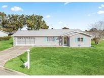 Gray house with teal accents, two-car garage, and spacious lawn at 9897 Se 178Th Pl, Summerfield, FL 34491
