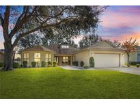 Charming single-story home featuring a well-manicured lawn, mature trees, and a two-car garage at 26709 Augusta Springs Cir, Leesburg, FL 34748