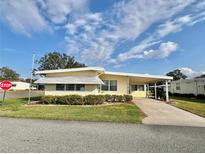 Front view of a yellow single-story home with carport and landscaping at 180 Hibiscus Way, Leesburg, FL 34748