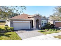 Charming single-story home with stone accents, brick driveway, manicured lawn, and attached two-car garage at 96 Silver Maple Rd, Groveland, FL 34736