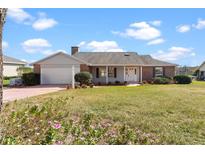 Charming single-story home featuring a well-manicured lawn, brick accents, attached garage, and inviting front porch at 1320 Cove Pl, Tavares, FL 32778