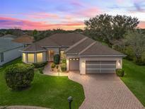 Aerial view of a lovely home with a well-manicured lawn, driveway and mature trees at sunset at 17652 Se 120Th Ter, Summerfield, FL 34491