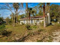 Charming home featuring a light yellow exterior, brown roof, and mature trees on a spacious lot at 18415 County Road 33, Groveland, FL 34736