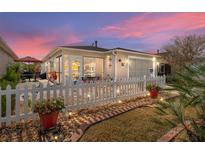 Charming home exterior with a white picket fence, patio, and manicured landscaping at sunset at 308 Emmalee Pl, The Villages, FL 32162