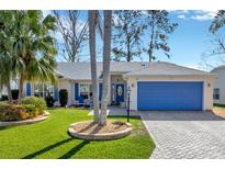 Charming single-story home featuring a vibrant blue garage door, lush landscaping, and a manicured lawn at 26148 Glen Eagle Dr, Leesburg, FL 34748