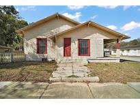 Charming single-story home featuring a covered porch, red door and window trim, and wood shingle siding at 401 S 6Th St, Leesburg, FL 34748